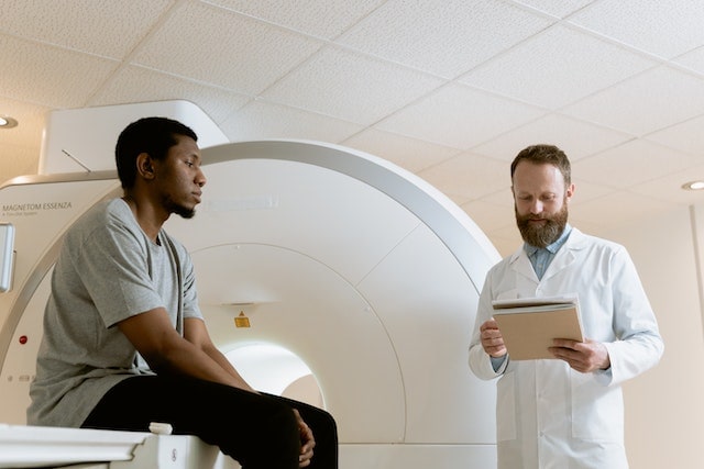 A Radiologist talking to his patient next to an MRI Machine.