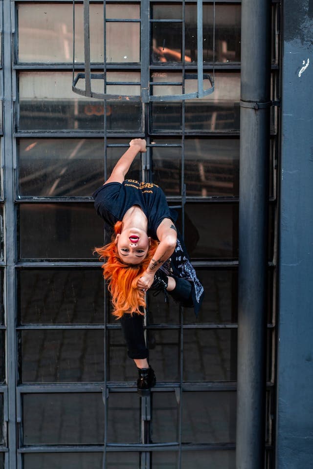 a girl upside down looking at the camera holding on a rope